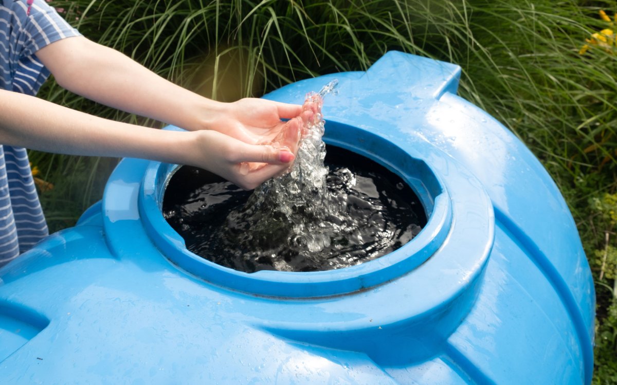 Frau hält Hände in Wasser einer blauen Regentonne