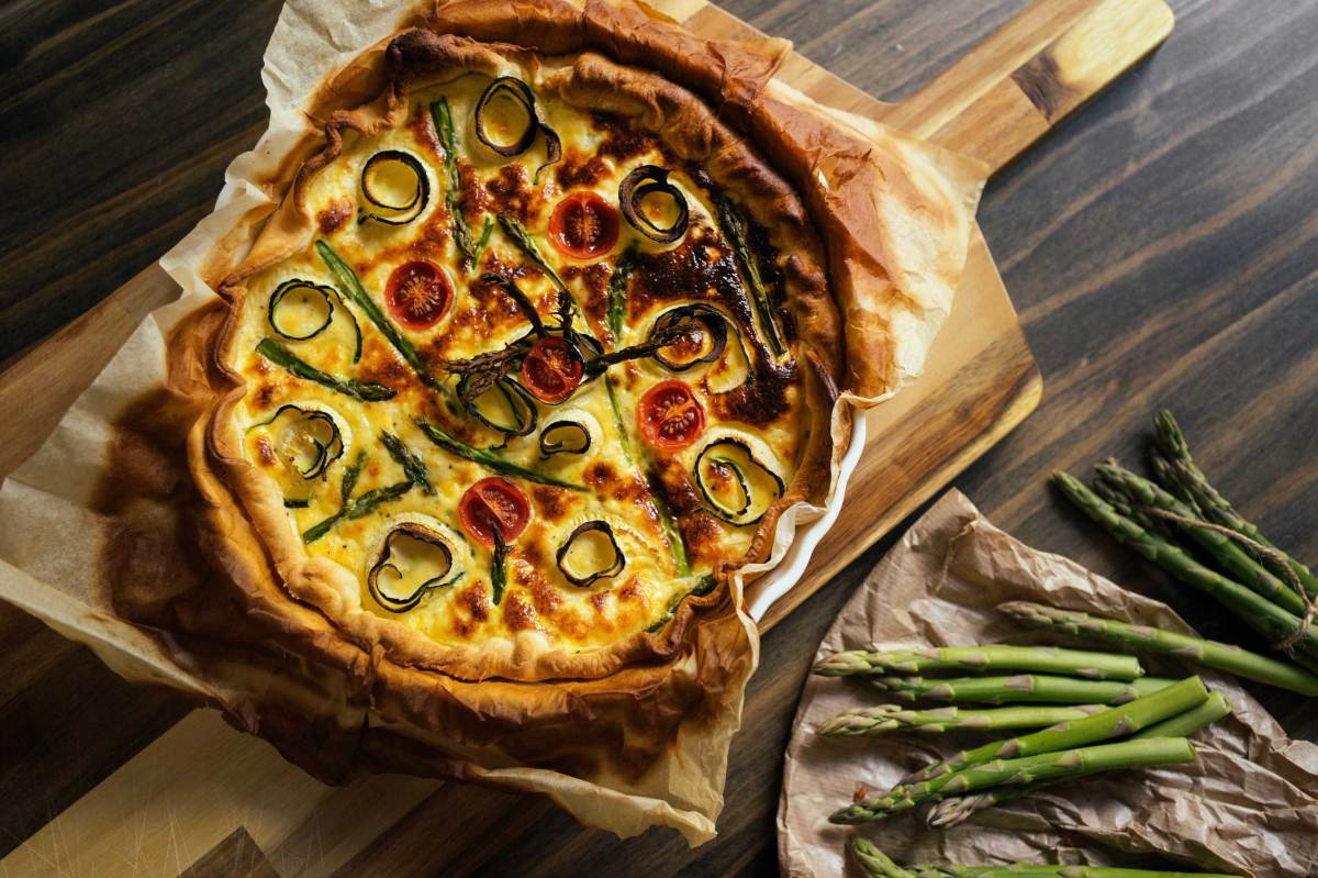 Appetitliche Quiche mit knusprigem Rand und buntem Gemüse, serviert auf rustikalem Untergrund.