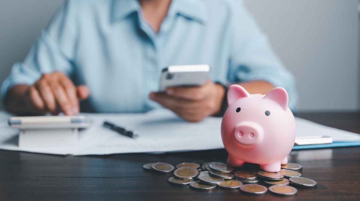 Frau sitzt vor einem Tisch mit einem rosa Sparschwein und Geld auf dem Tisch.