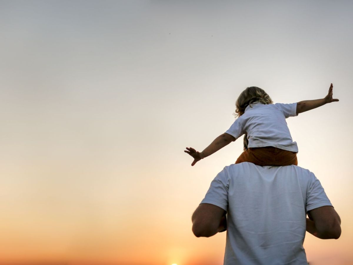 Ein Vater trägt sein Kind auf den Schultern im Sonnenuntergang