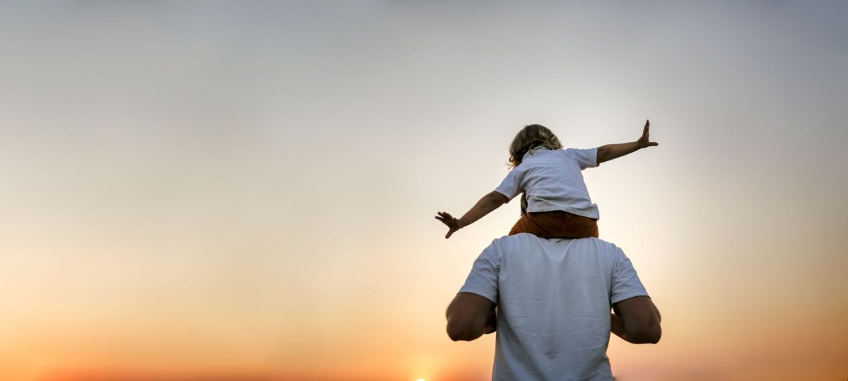 Ein Vater trägt sein Kind auf den Schultern im Sonnenuntergang