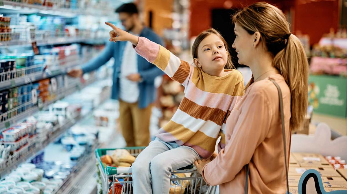 Mutter und Tochter stehen im Supermarkt vor einem Kühlregal. Die Tochter zeigt auf etwas, das sie haben möchte.