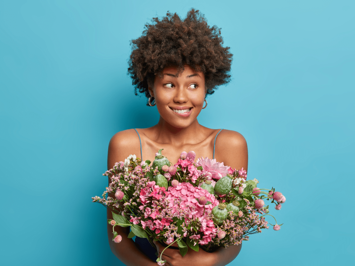 Frau mit blumen vor einer blauen Wand, die nervös zur Seite schaut.