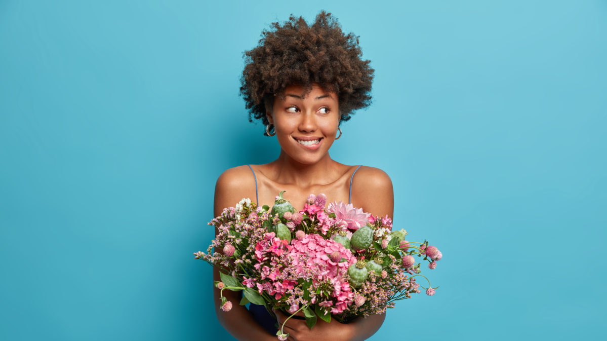 Frau mit blumen vor einer blauen Wand, die nervös zur Seite schaut.