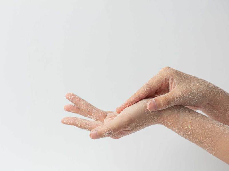 Frau, die ein natürliches Salzpeeling auf die Hände aufträgt, vor weißem Hintergrund