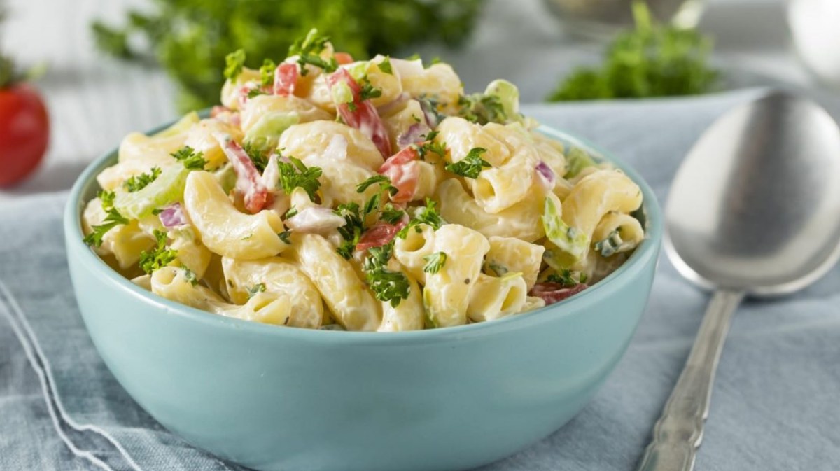 Nudelsalat in einer hellblauen Schüssel mit Petersilie und Speck.