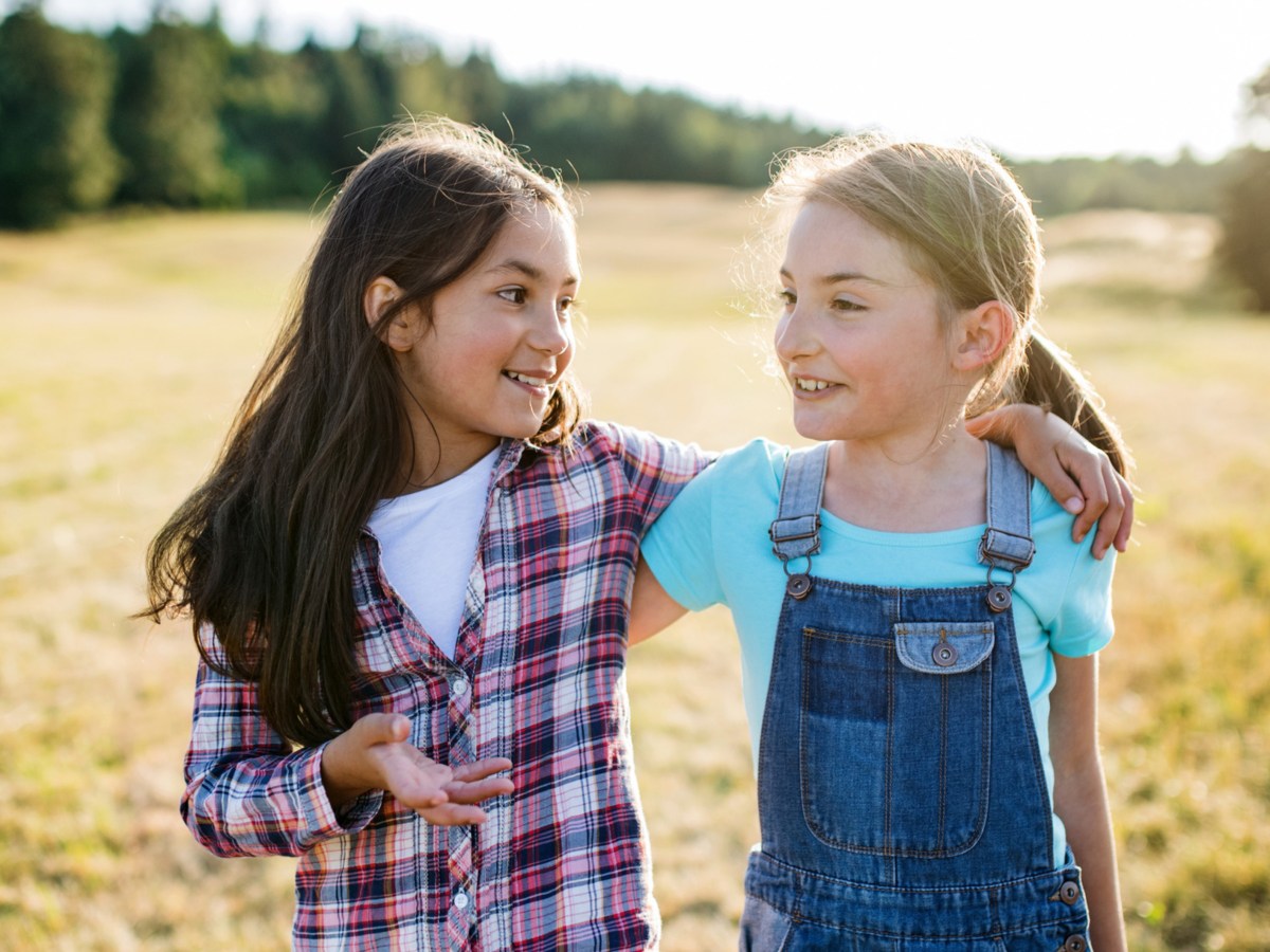 Zwei junge Mädchen laufen durch Feld und reden miteinander.