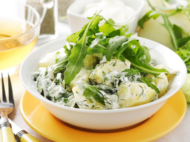 Kartoffelsalat mit Joghurtdressing und Rucola in weißer Schüssel.