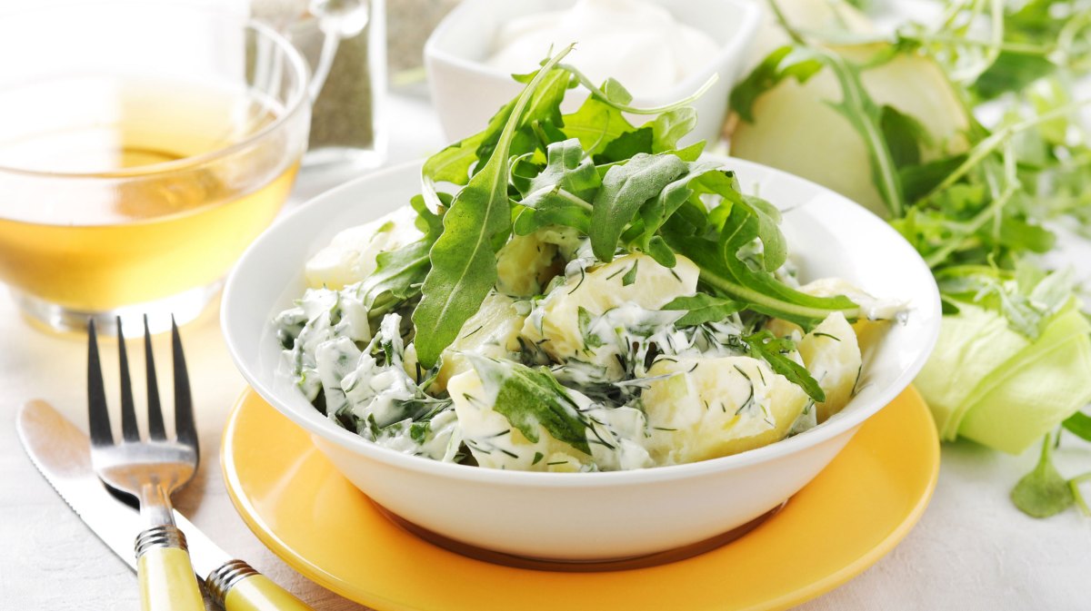 Kartoffelsalat mit Joghurtdressing und Rucola in weißer Schüssel.