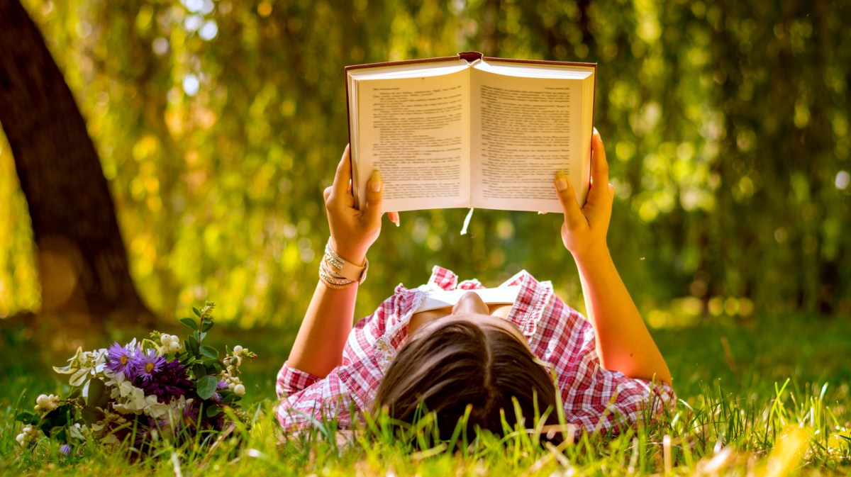 Frau liegt auf Wiese und liest Buch.