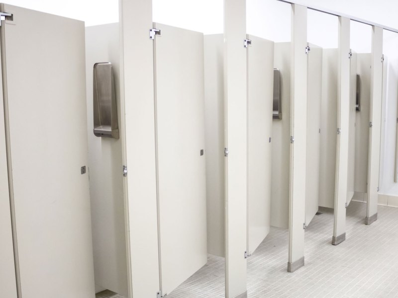 Öffentliche Toilette mit mehreren Kabinen, die alle ein Stück geöffnet sind.