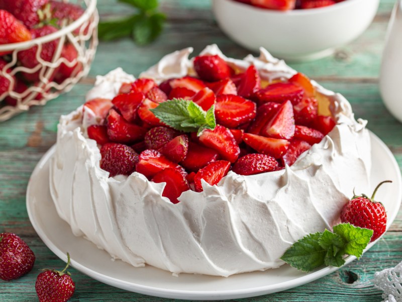 Pavlova mit frischen Erdbeeren auf gedecktem Tisch.