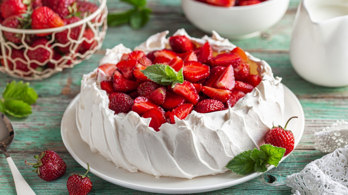 Pavlova mit frischen Erdbeeren auf gedecktem Tisch.