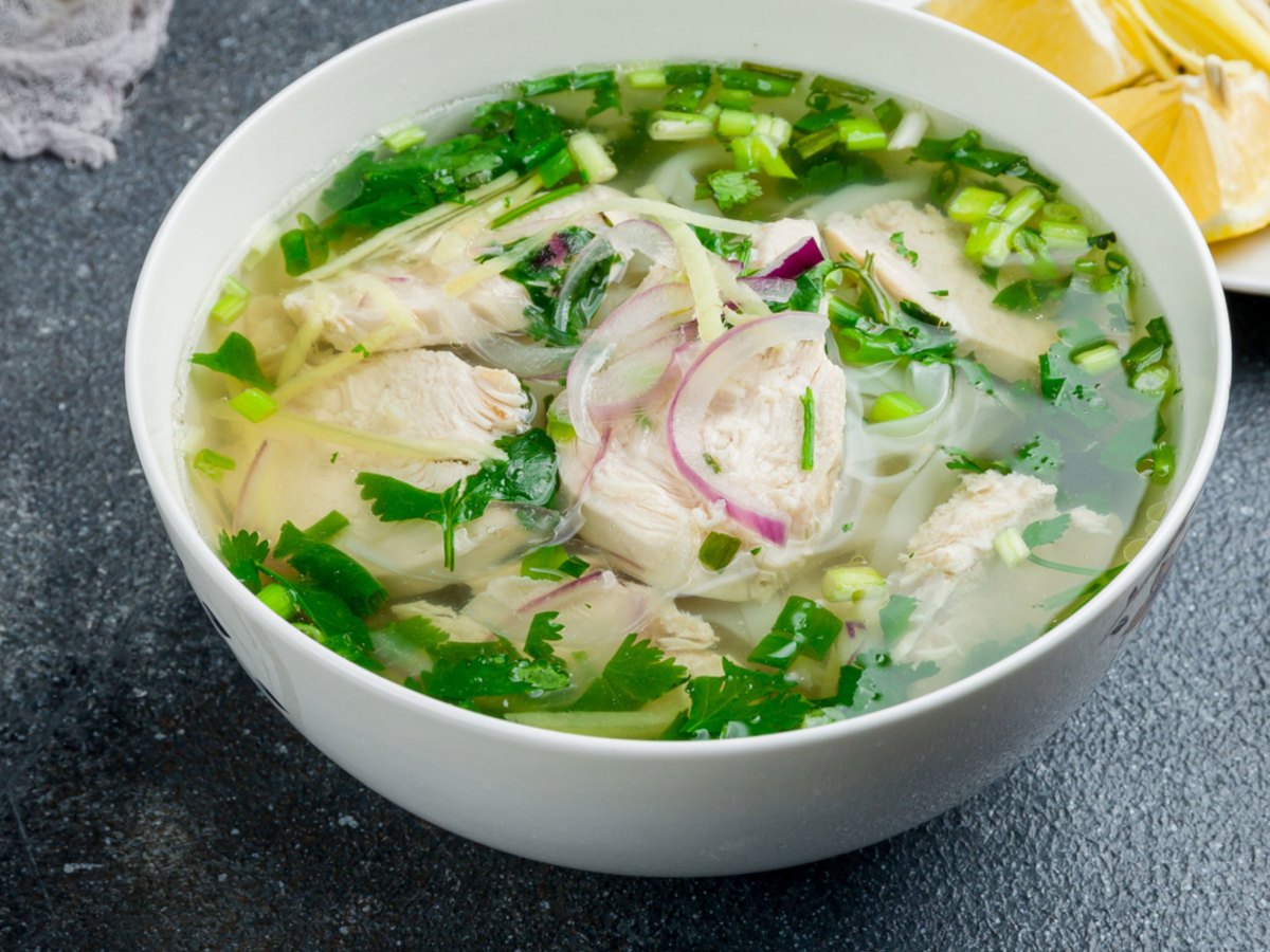 Pho ga Suppe in einer weißen Schüssel mit Zutaten, die da rum verstreut wurden.