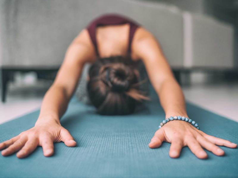 Yoga zu Hause, Stretching, Meditation Frau macht Kinder Pose. Hände berühren Boden Übungsmatte und Mala-Armband. Fitness, Entspannung, stressfrei