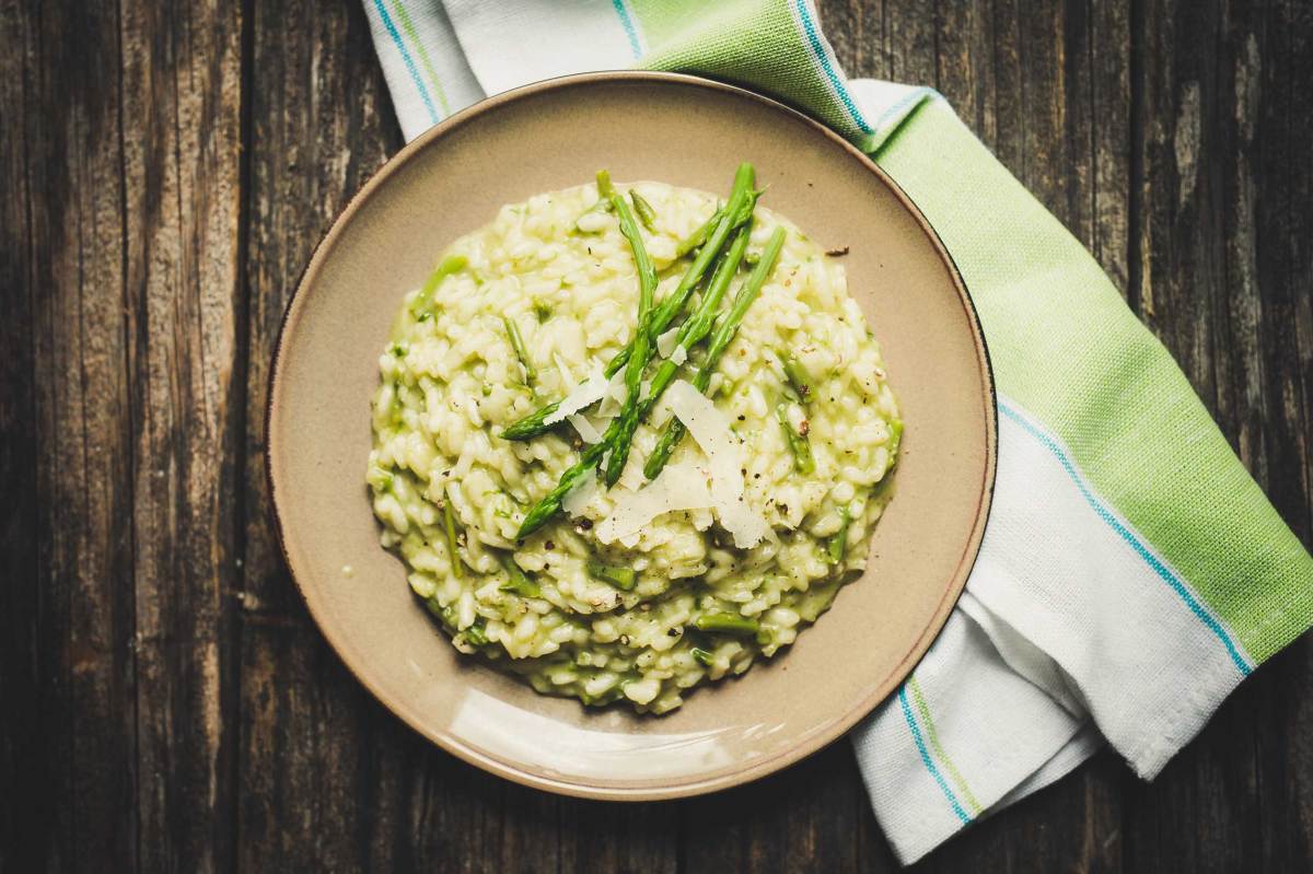 Cremiges Spargelrisotto mit geriebenem Parmesan auf einem braunen Teller, angerichtet auf einem dunklen Holztisch mit grün-weißer Serviette.