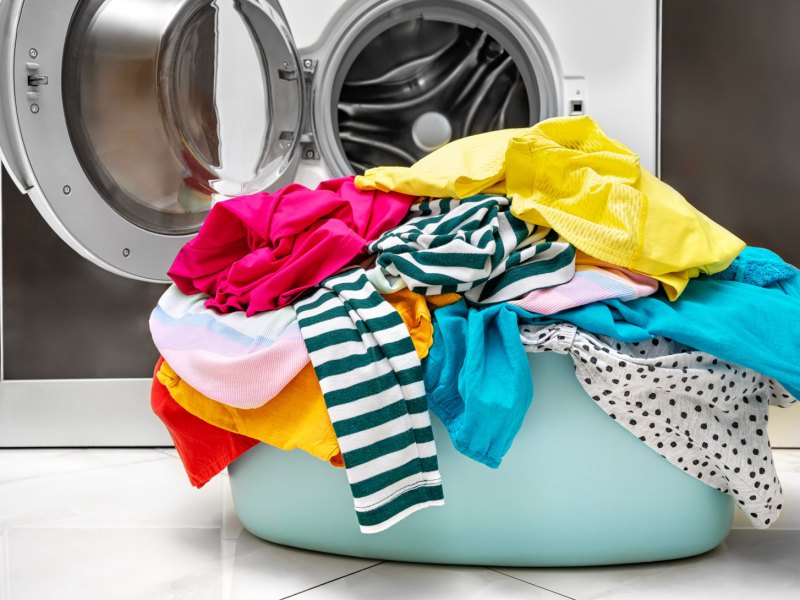 Wäschekorb mit Wäsche vor Waschmaschine als Smybolbild für "Wäsche stinkt nach dem Waschen"