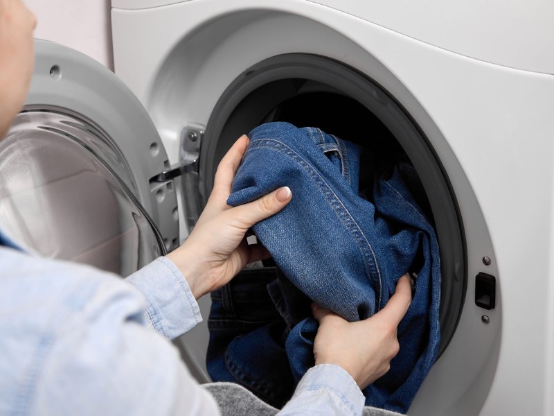 Frau, die eine Waschmaschine mit Jeanshosen befüllt