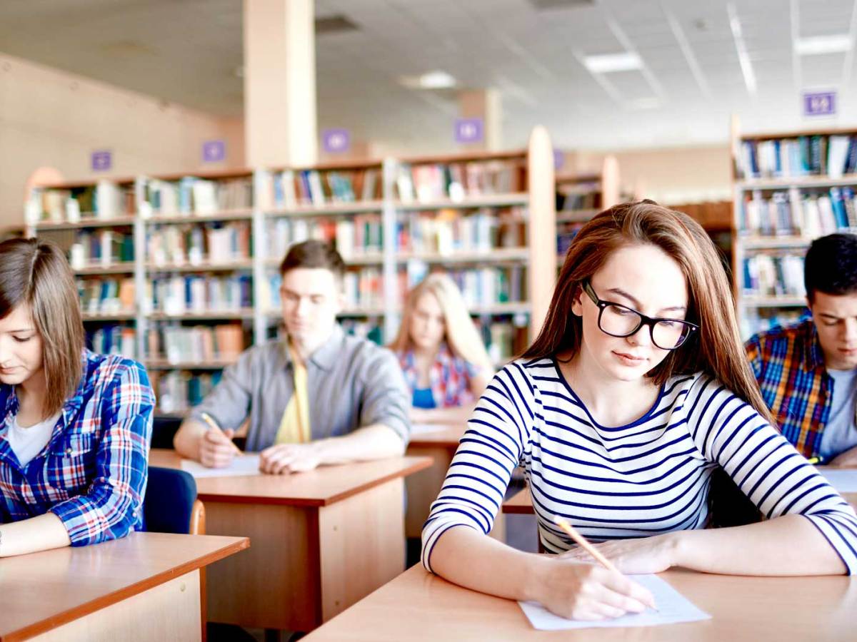 Schüler*innen sitzen an kleinen Einzeltischen und schreiben eine Abschlussarbeit.