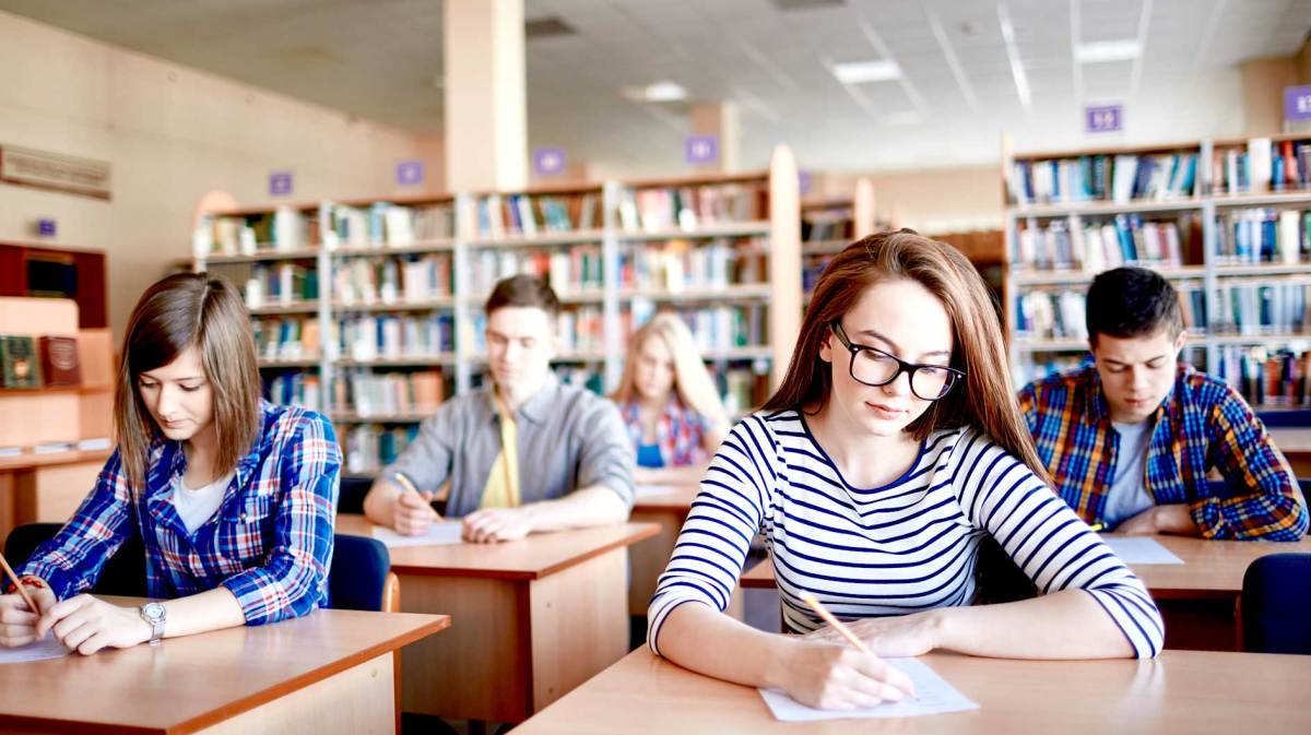 Schüler*innen sitzen an kleinen Einzeltischen und schreiben eine Abschlussarbeit.