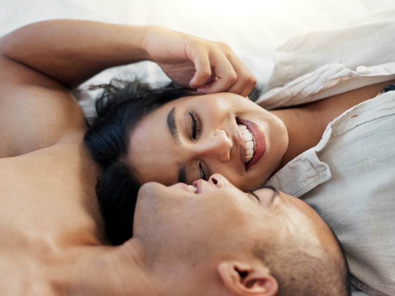 Mann und Frau im Bett, die sich gegenseitig verliebt in die Augen schauen und anlächeln.