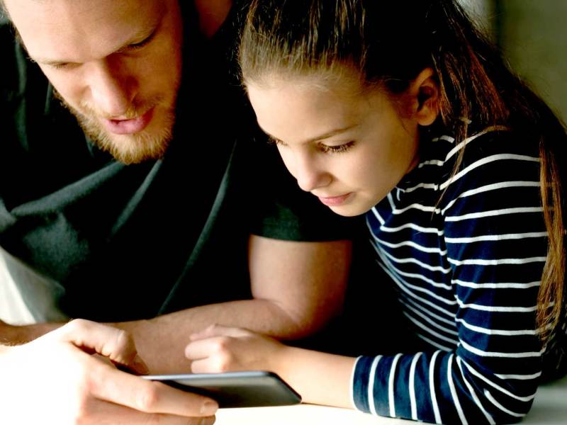 Vater und Tochter schauen sich gemeinsam etwas auf einem Handy an.