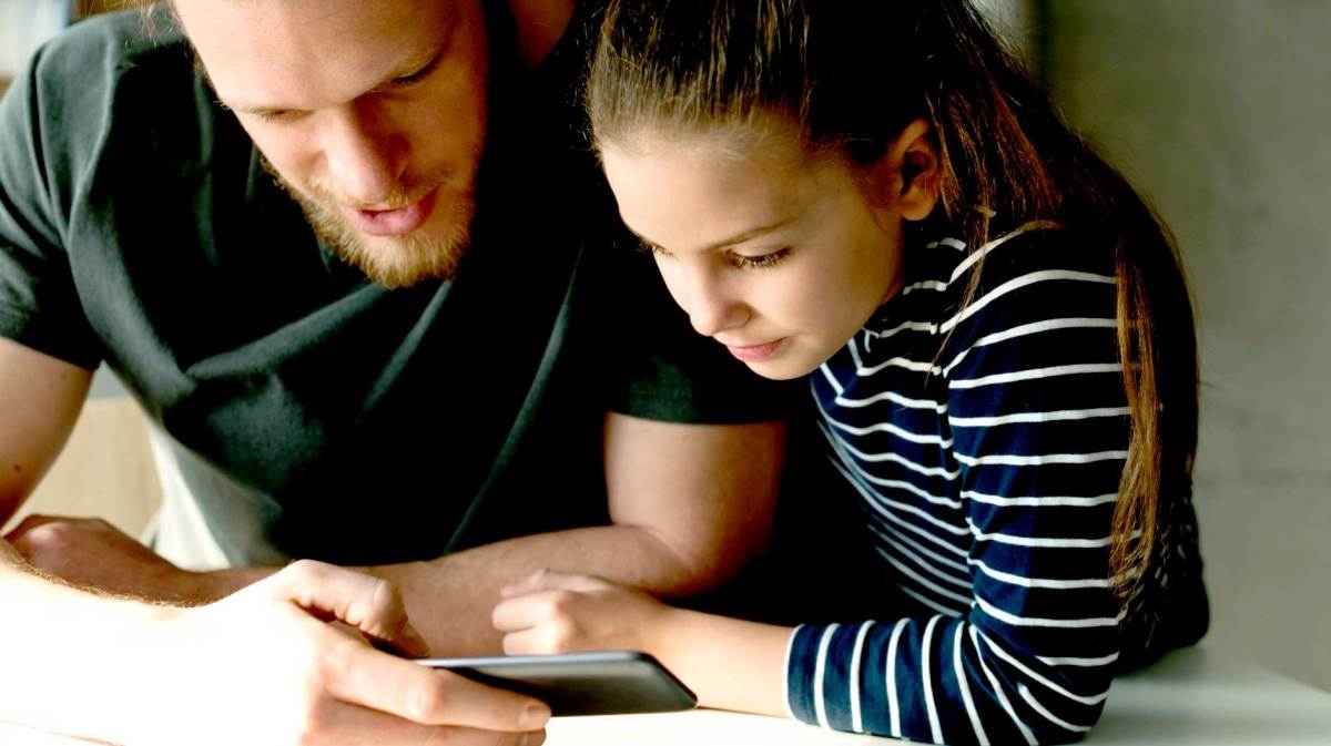 Vater und Tochter schauen sich gemeinsam etwas auf einem Handy an.