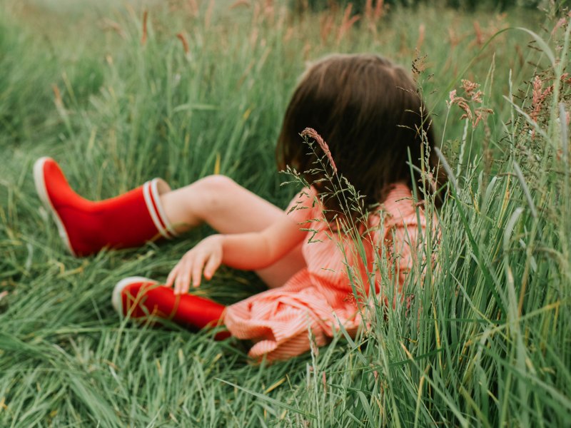 Kind mit roten Gummistiefeln liegt im Gras.
