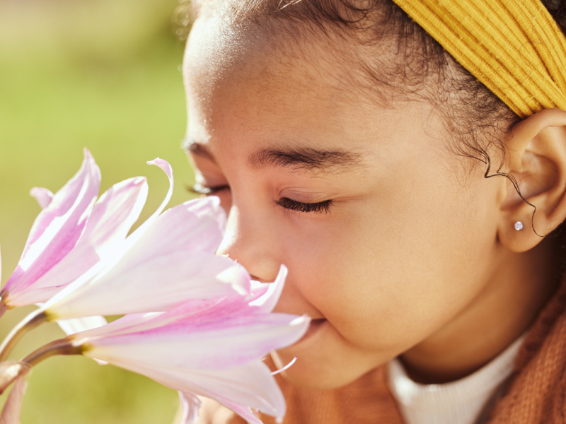 Kind vor einer Blume, das mit geschlossenen Augen daran riecht.