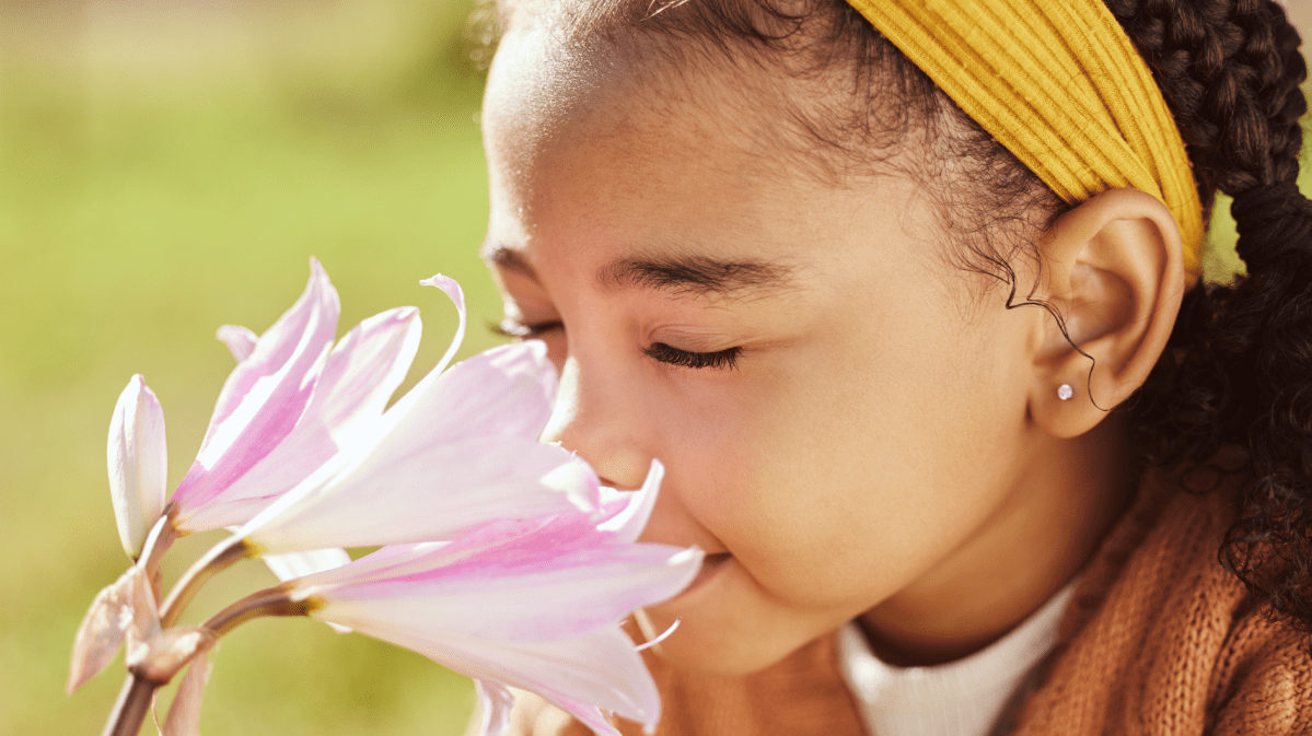 Kind vor einer Blume, das mit geschlossenen Augen daran riecht.