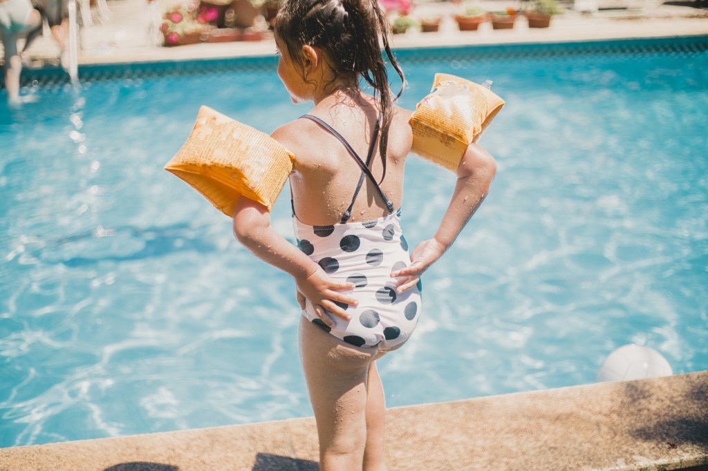 Mädchen mit Schwimmflügeln vor Schwimmbecken.