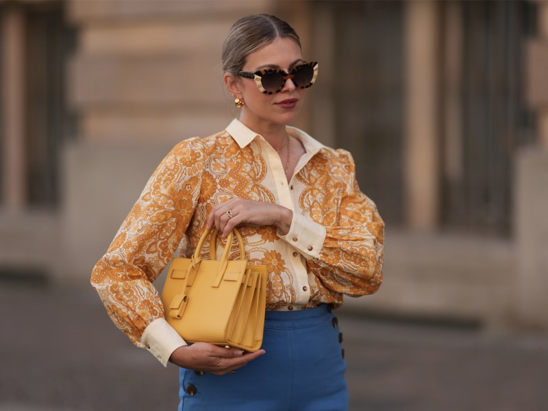 Aline Kaplan mit großer Sonnenbrille, goldenen Ohrringen und gelber Tasche