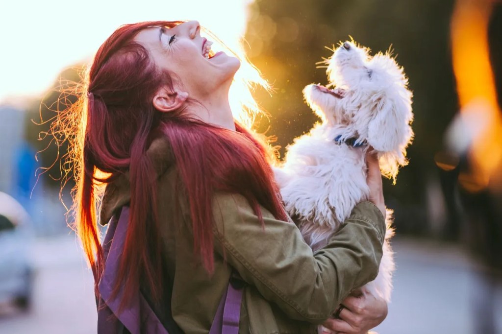 Frau mit Hund auf dem Arm, die lacht und nach oben schaut.