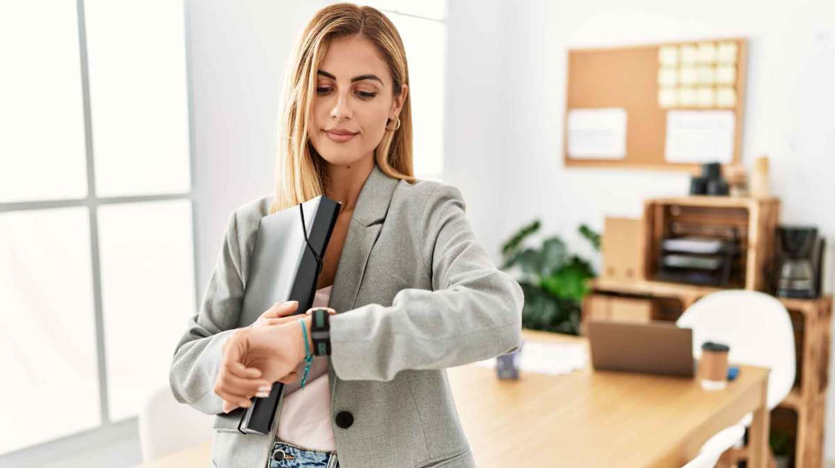 Junge Frau ist im Büro und guckt auf die Uhr.