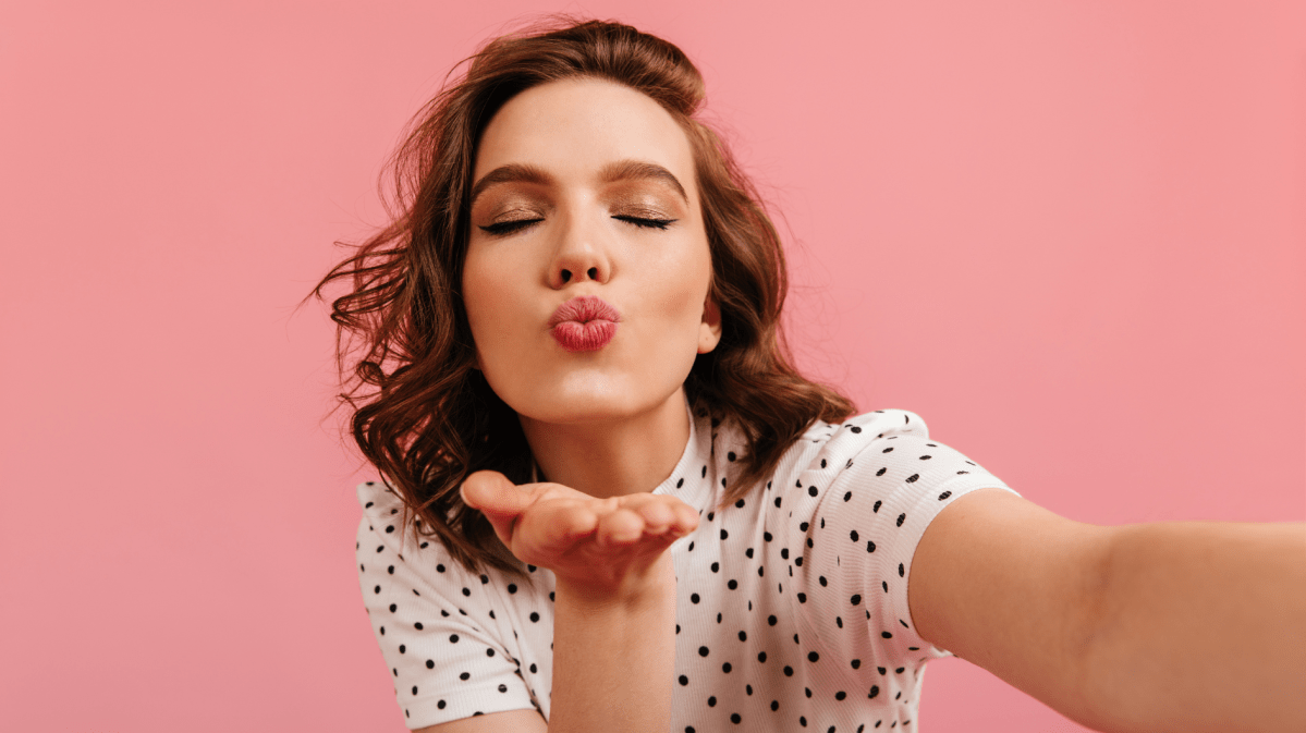 Frau mit Kussmund vor einer rosa Wand.