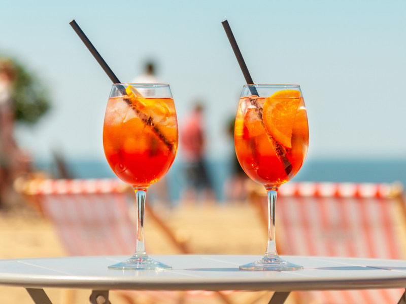 Zwei Cocktailgläser auf Tisch vor sommerlichem Hintergrund.