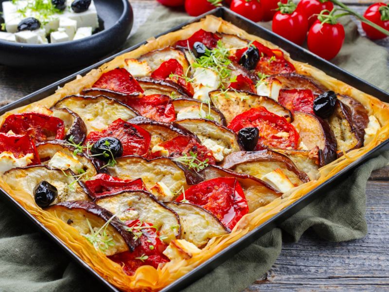 Tarte auf einem Backblech mit Auberginen, Tomaten und Oliven.