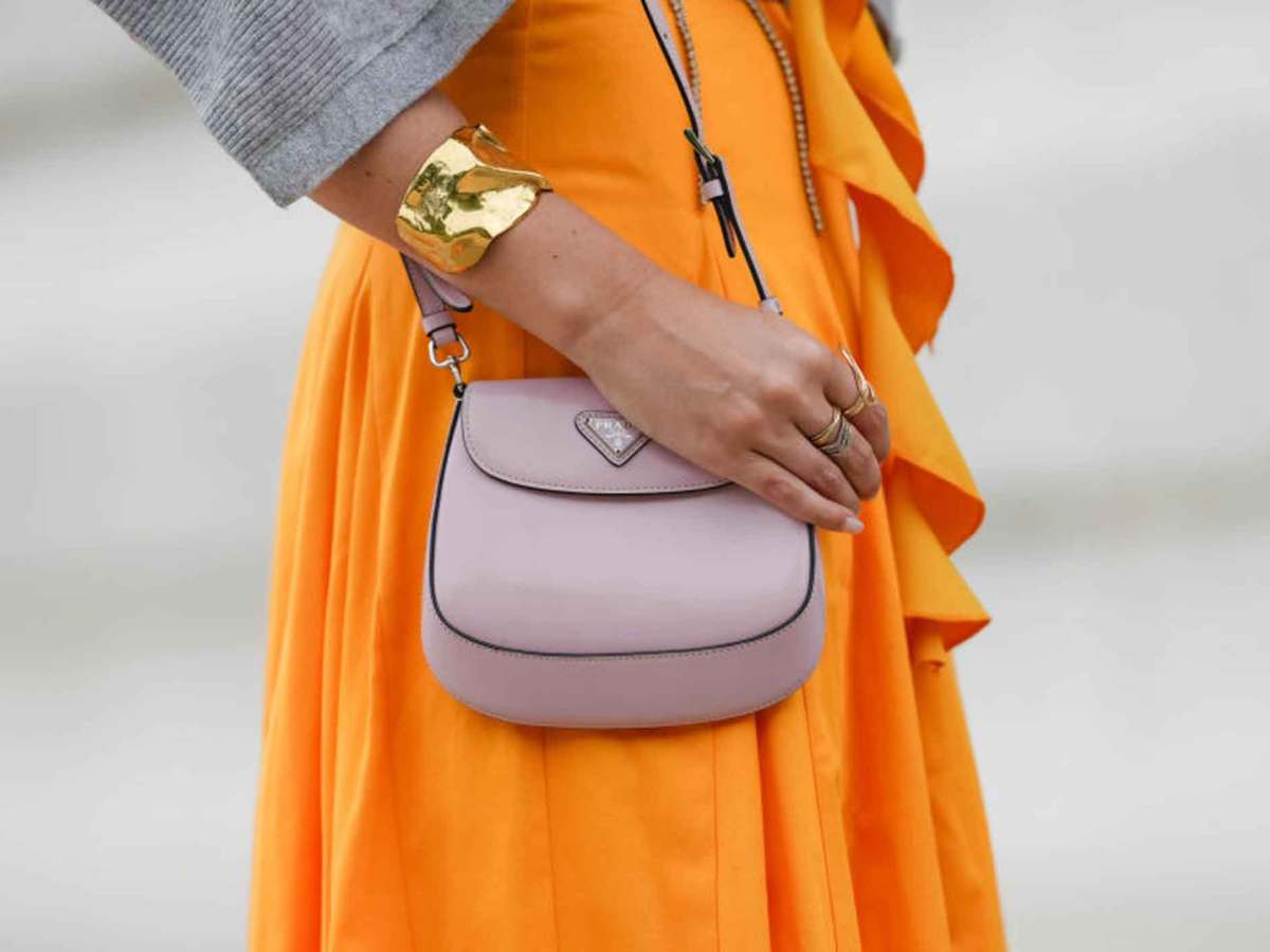 Frau mit orange-farbenem Kleid trägt eine rosa Tasche.