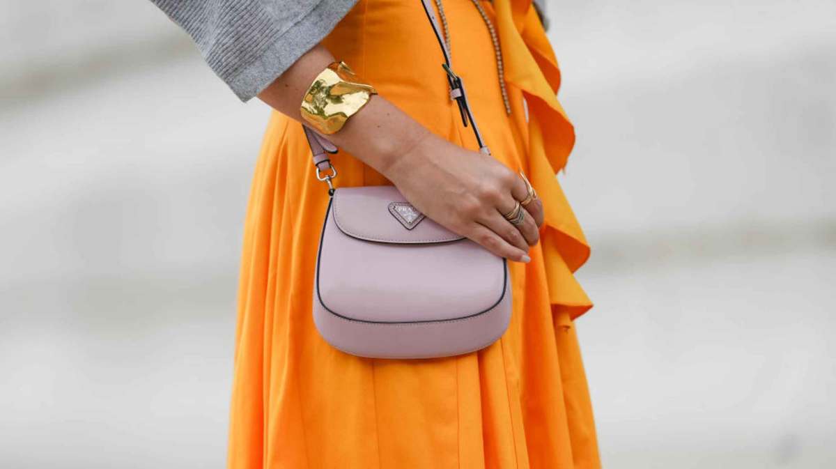 Frau mit orange-farbenem Kleid trägt eine rosa Tasche.