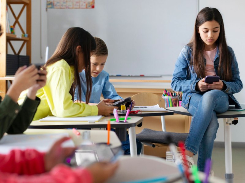 Gruppe von Schülern im Klassenzimmer. Alle hängen einzeln am Handy, es findet kein Austausch zwischen ihnen statt.