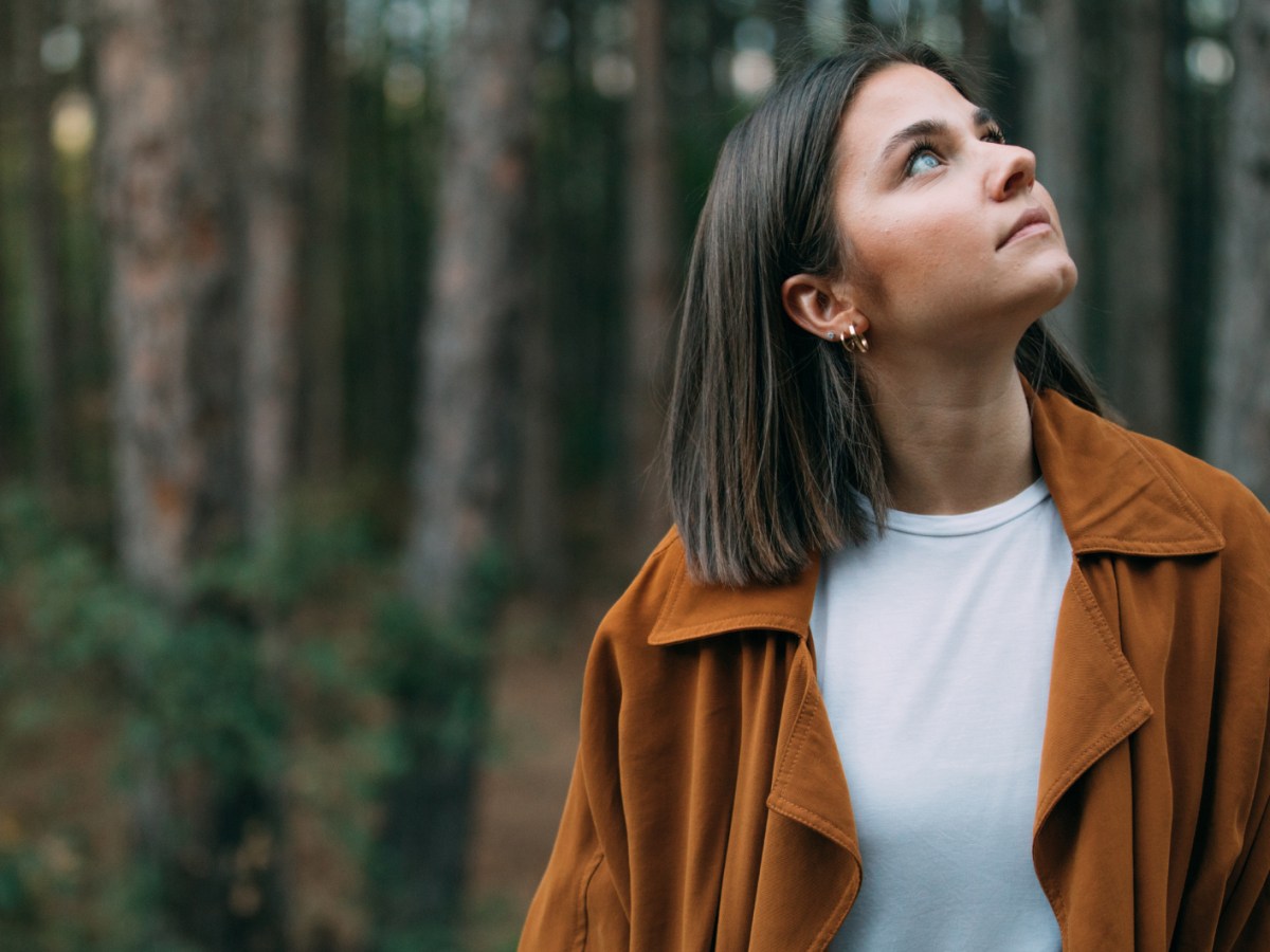 Junge Frau steht im Wald und schaut nach oben.