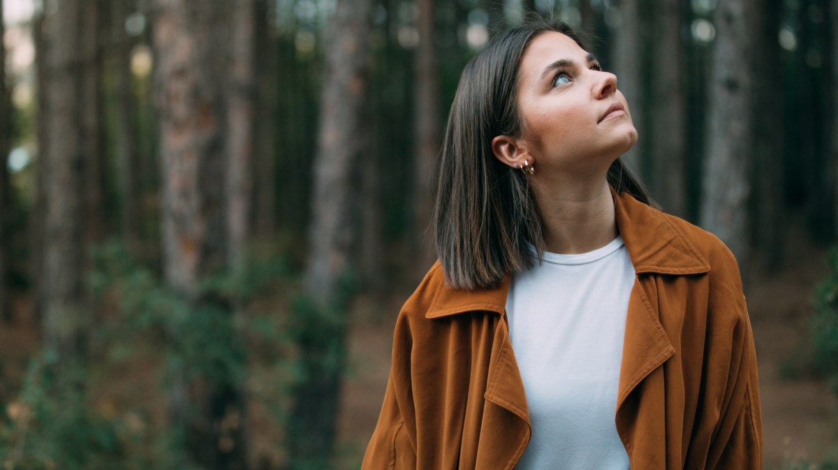 Junge Frau steht im Wald und schaut nach oben.