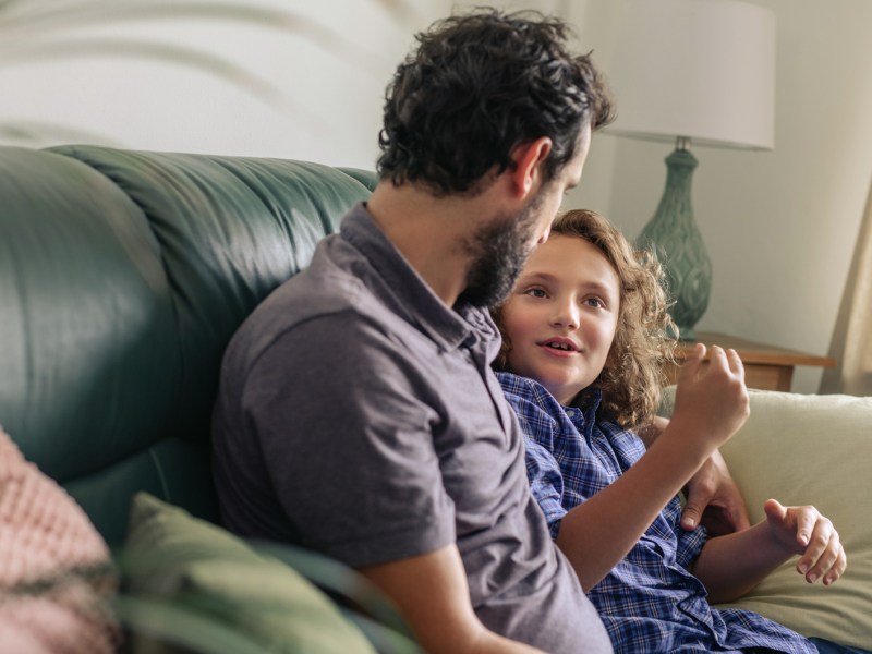 Vater und Kind sitzen auf dem Sofa und quatschen ganz entspannt.