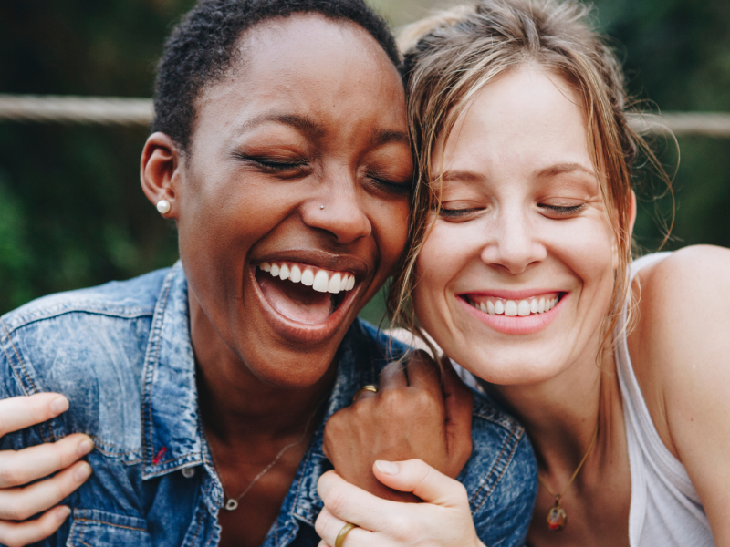 Zwei Frauen auf einer Bank draußen, die sich umarmen und lachen.