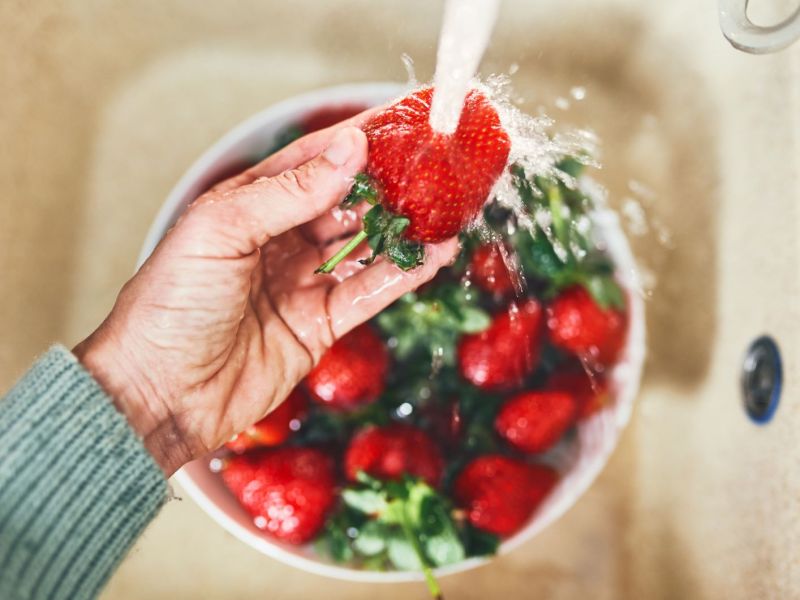 Eine Hand wäscht Erdbeeren unter Wasser ab