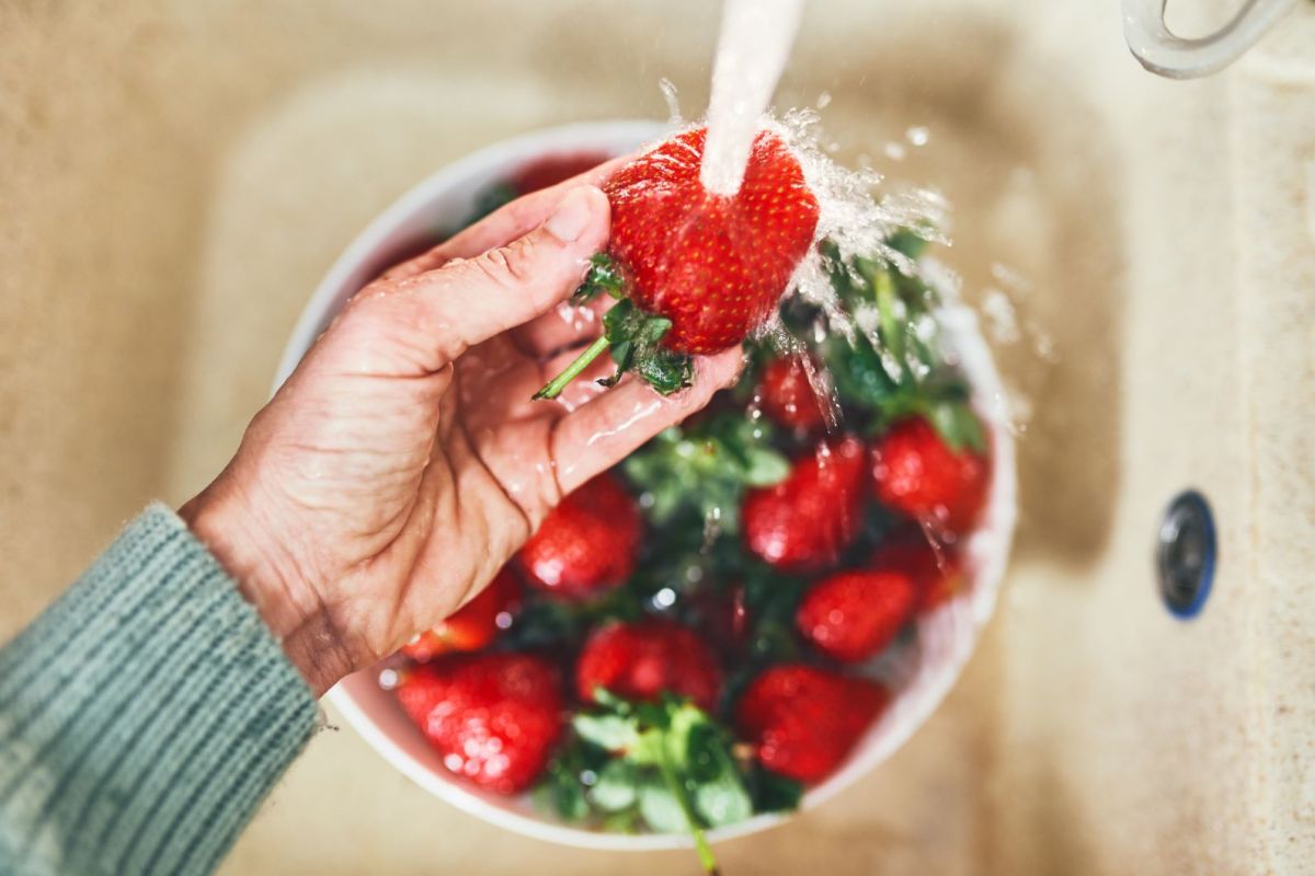 Eine Hand wäscht Erdbeeren unter Wasser ab