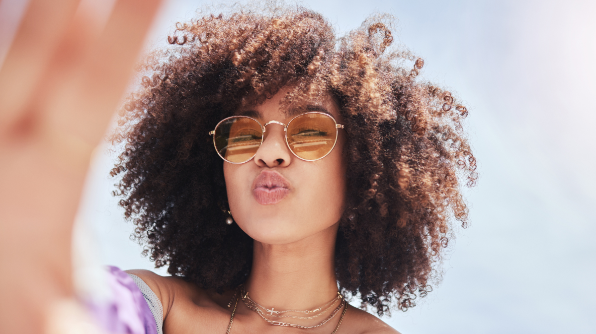 Frau, die ein Duckface macht und eine Sonnenbrille aufhat, während sie ein Selfie macht.