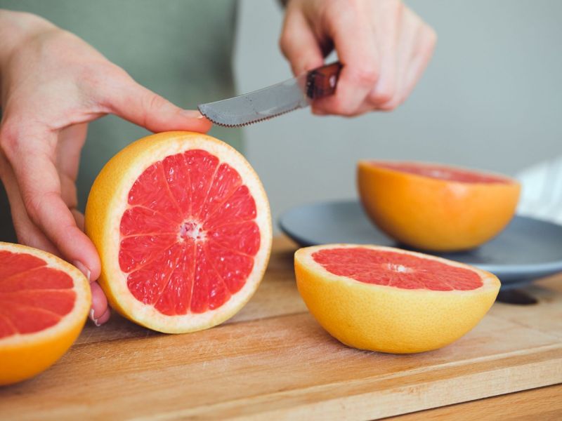 Eine Person schneidet eine Grapefruit mit einem Messer auf.