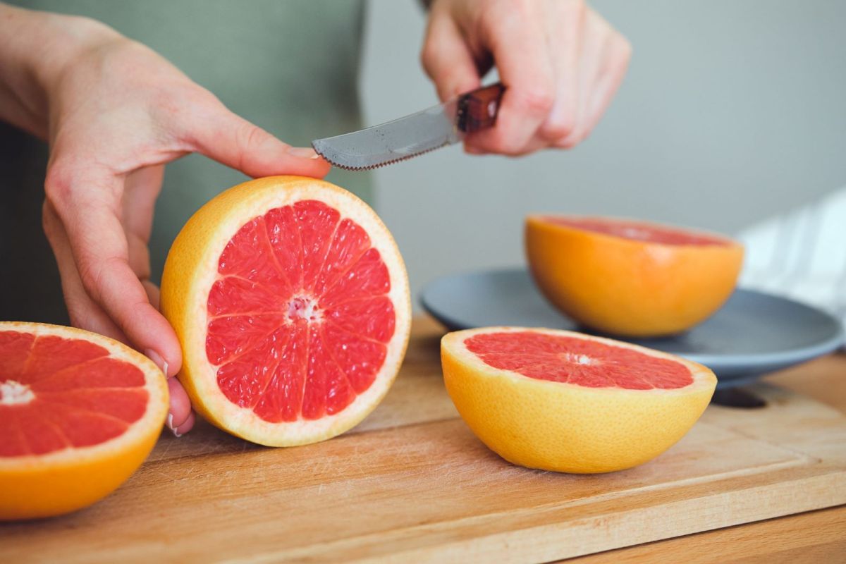 Eine Person schneidet eine Grapefruit mit einem Messer auf.