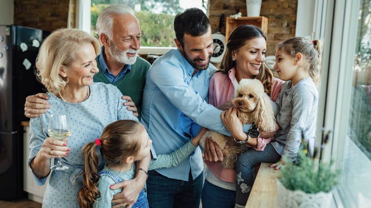 Zwei Enkel, Eltern, Großeltern und der Familienhund sind in der Küche und stoßen gemeinsam an.